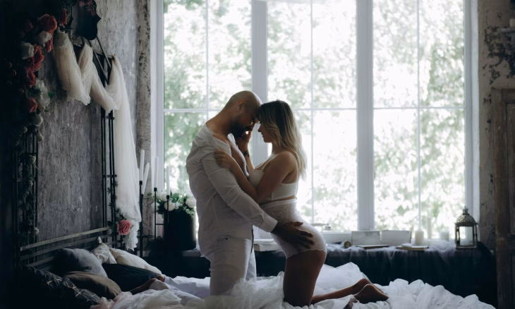 man and woman kneeling on bed beside window
