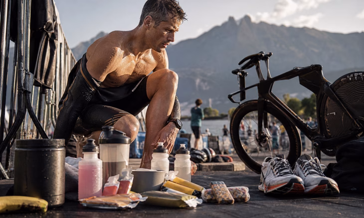 Un triathlète se ravitaille près de son vélo, avec des chaussures et des aliments devant un paysage montagneux